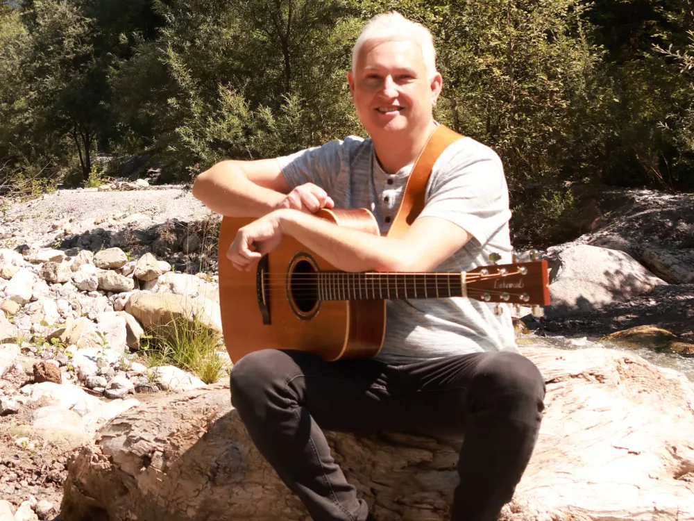 „Alfred Bischof mit Gitarre am Bach im Galinawald – musizierend inmitten der Natur“